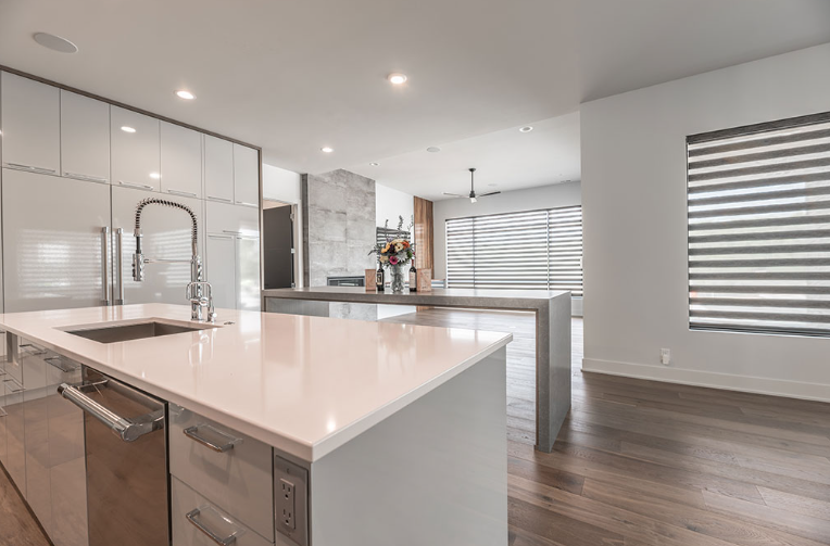Modern kitchen with a large island, white countertops, and wood flooring.