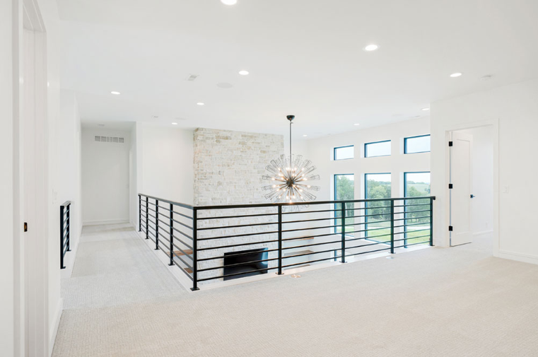 Bright, modern interior with a balcony, black railing, and a decorative chandelier.
