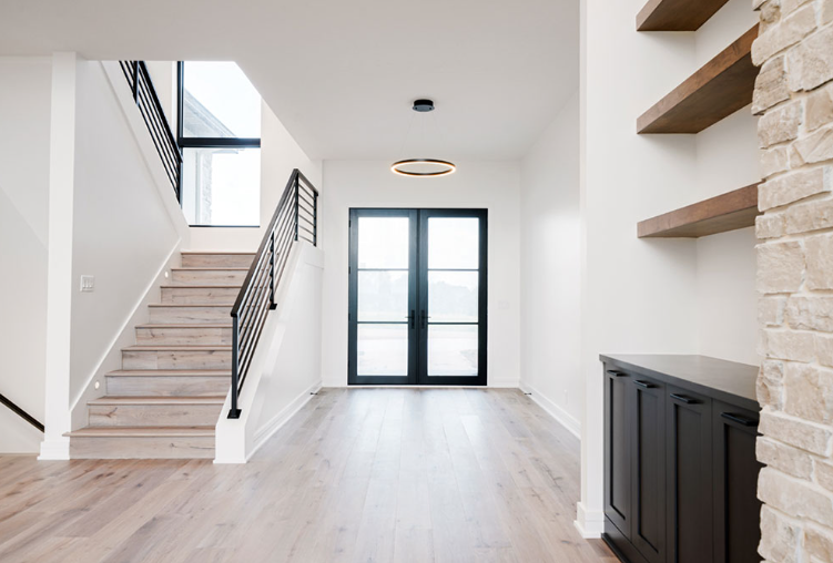 Bright modern home entryway with staircase, black door, and floating shelves.