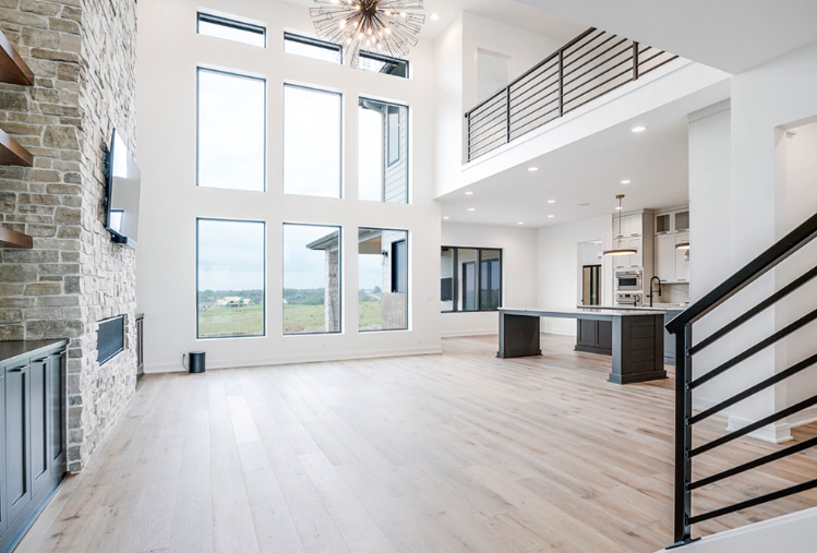 Spacious modern living room with tall windows, hardwood floors, and a stone accent wall.
