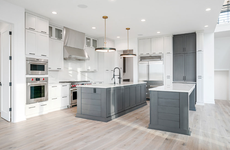 Modern white and gray kitchen with two islands, stainless steel appliances, and wood flooring.
