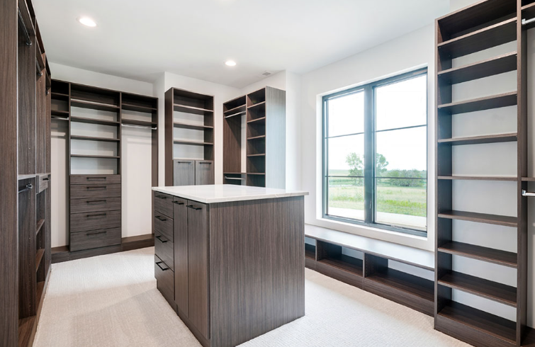 Walk-in closet with dark wood shelving, drawers, and an island with a window and white floor.