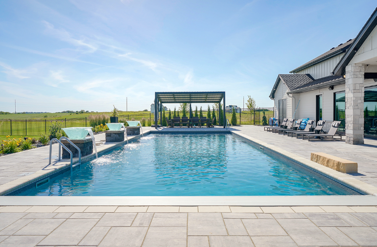 Swimming pool with pergola, chairs, and modern house on a sunny day.