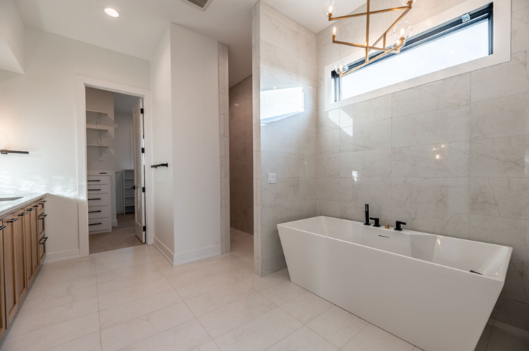 Modern white bathroom with a tub, shower, and walk-in closet.