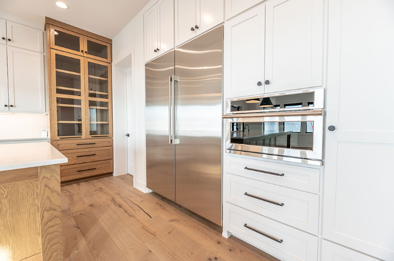 Kitchen with stainless steel refrigerator and built-in white oven and cabinets, wood floors.