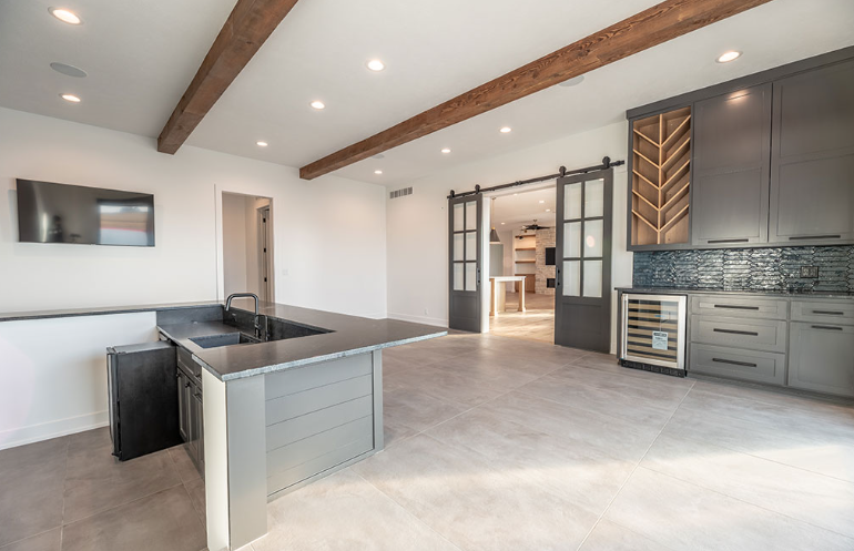 Modern kitchen with a gray island, cabinets, and sliding doors. Wooden beams and accents.