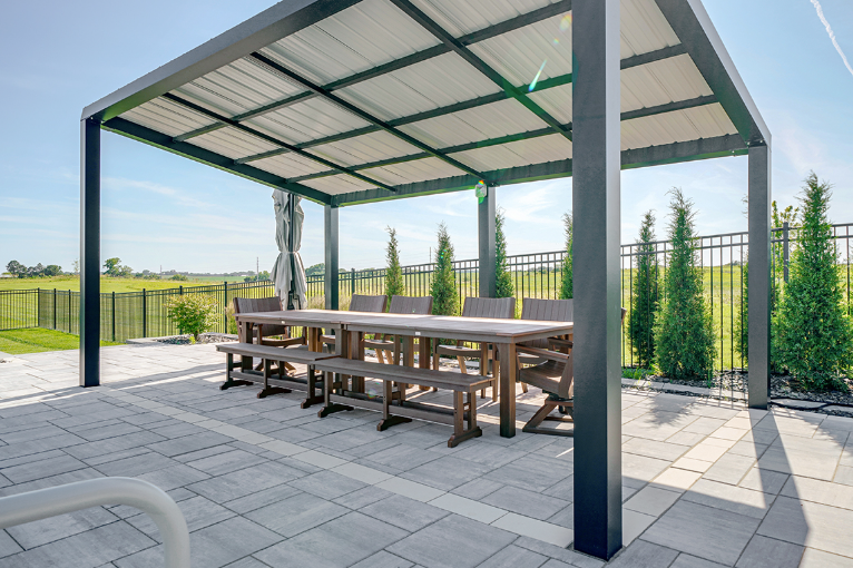 Outdoor patio with a long wooden table, benches, and a metal pergola roof.