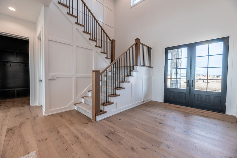Entryway with wooden floors, staircase, and double doors; white walls, dark gray trim.