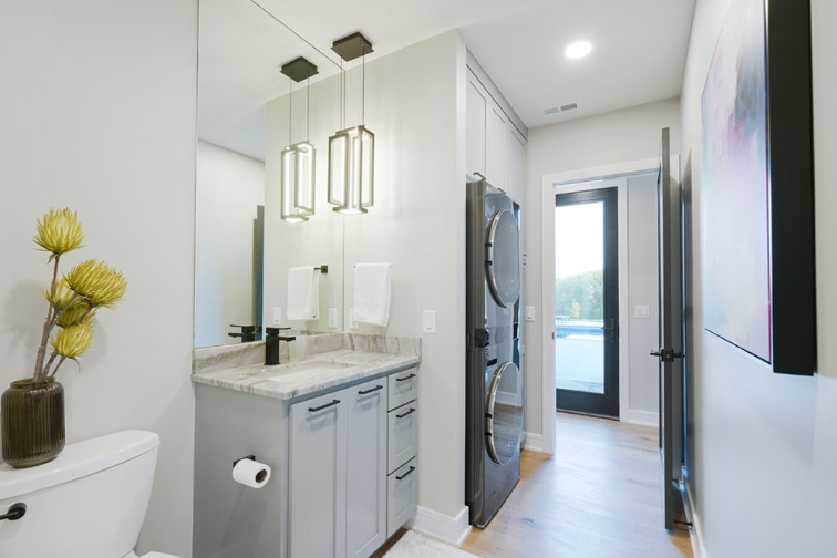 Modern powder room with gray cabinetry, a marble countertop, and a stackable washer and dryer.