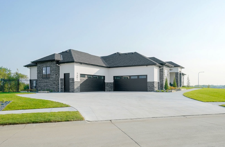 Modern house with a light-colored exterior, black garage doors, and a concrete driveway.