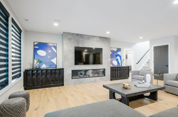 Modern living room with fireplace, TV, grey furniture, abstract blue art, and light wood floors.