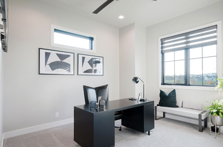 Modern home office with black desk, artwork, and window with blinds.