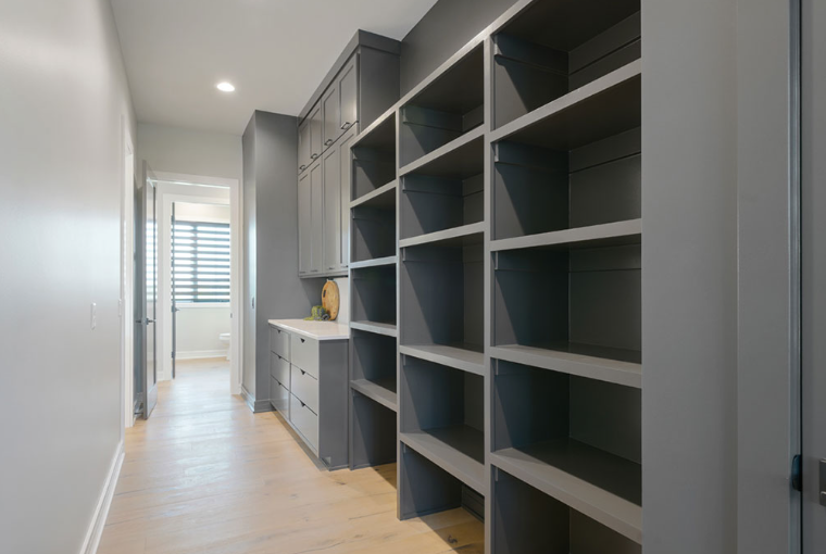 Gray built-in shelving and cabinets in a narrow hallway. Light wood floor and gray walls.