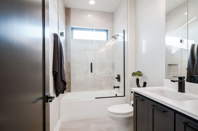 Modern bathroom with black accents: dark cabinets, fixtures, shower door, and towel. White walls, tub, and toilet.