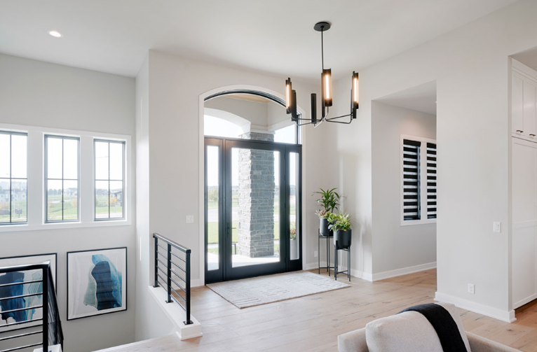Spacious, light-filled entryway with black door, chandelier, and modern staircase.