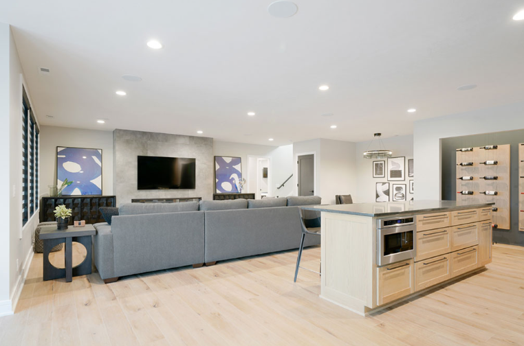 Open-concept living space with gray sectional, kitchen island, built-in wine storage, and modern artwork.