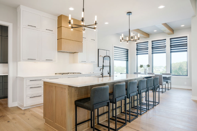 Modern kitchen with light wood island, white cabinets, and dark stools.