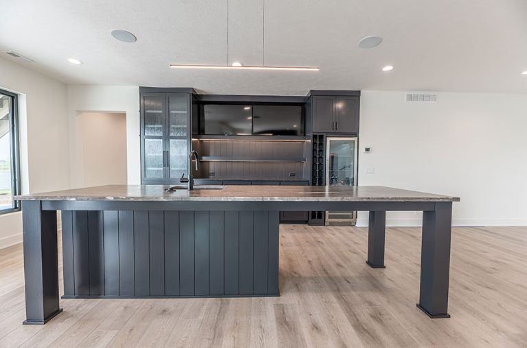 Dark gray kitchen island with dark gray cabinets in a modern, light-filled room.