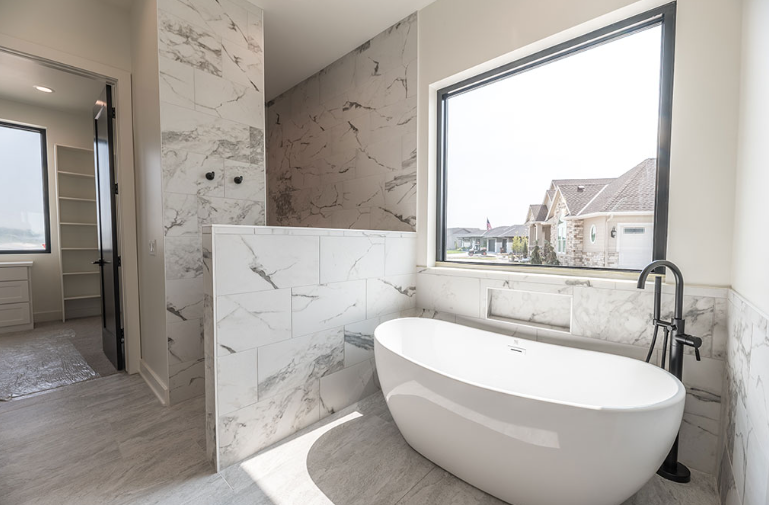 Bathroom with marble tile walls, a freestanding tub, and a window with a view.