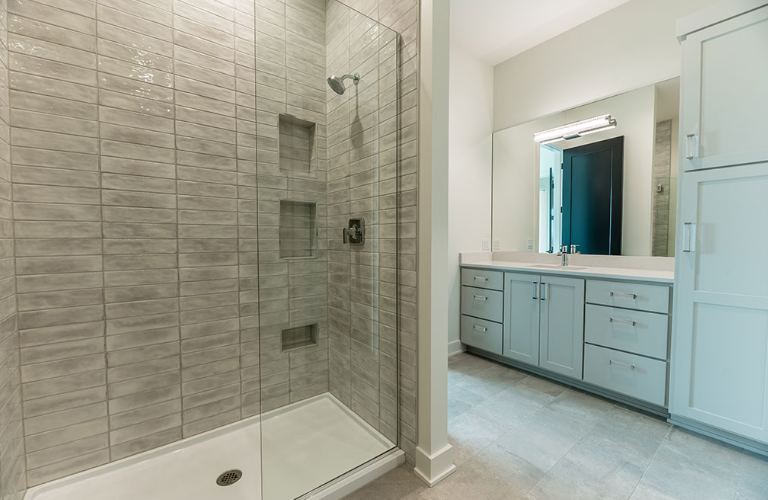 Modern bathroom with a tiled shower, vanity, and storage cabinets in light colors.