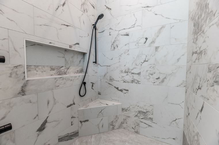 White marble-tiled shower with a black showerhead, shelf, and bench.