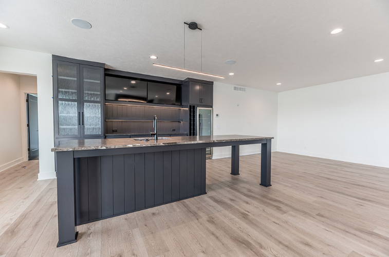 Modern kitchen island with dark cabinets and countertop, light wood floor, white walls.