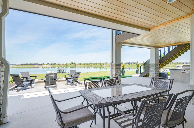 Patio with outdoor furniture overlooking a lake, under a covered deck.