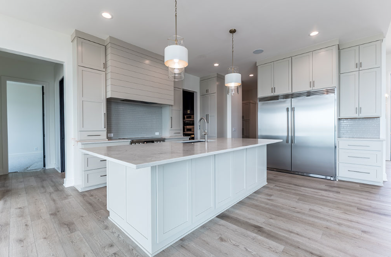 Modern white kitchen with island, stainless steel refrigerator, and pendant lights.