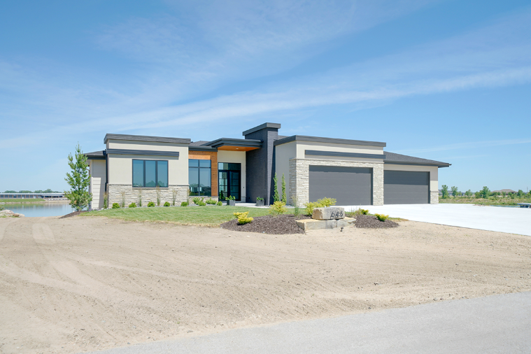 Modern single-story home with a grey exterior, two-car garage, and landscaped front yard under a blue sky.