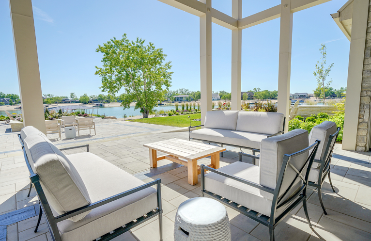 Patio with white outdoor furniture, overlooking a lake on a sunny day.