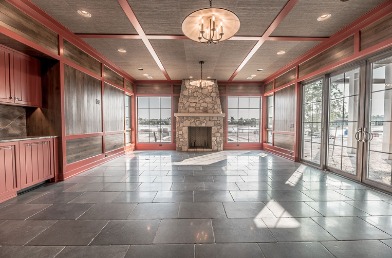 Spacious room with fireplace, gray tiled floor, large windows, and reddish-brown trim.
