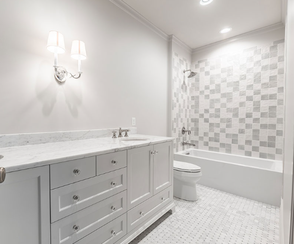 White bathroom with vanity, toilet, bathtub with mosaic tiled wall and recessed lighting.
