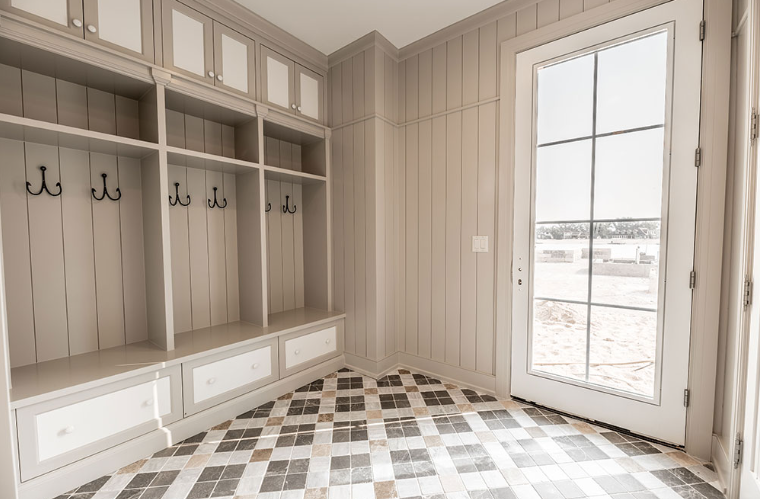 Mudroom with built-in storage, hooks, and a tiled floor. A glass door lets in sunlight.