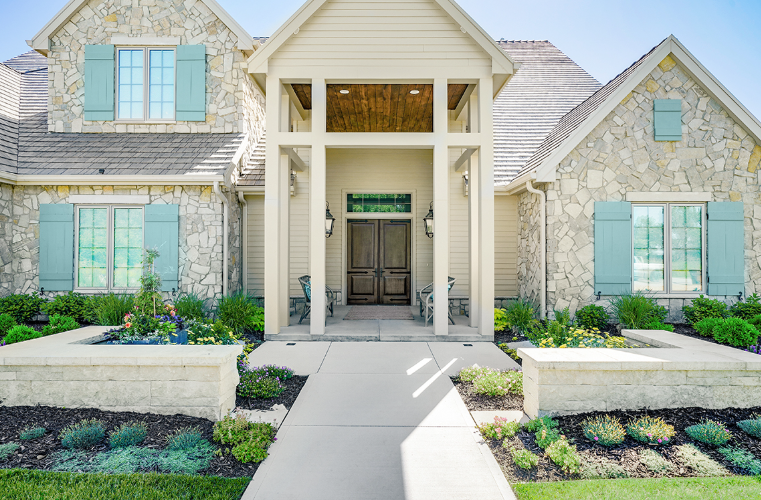 Stone facade house with blue shutters, beige trim, and a concrete path leading to double doors.