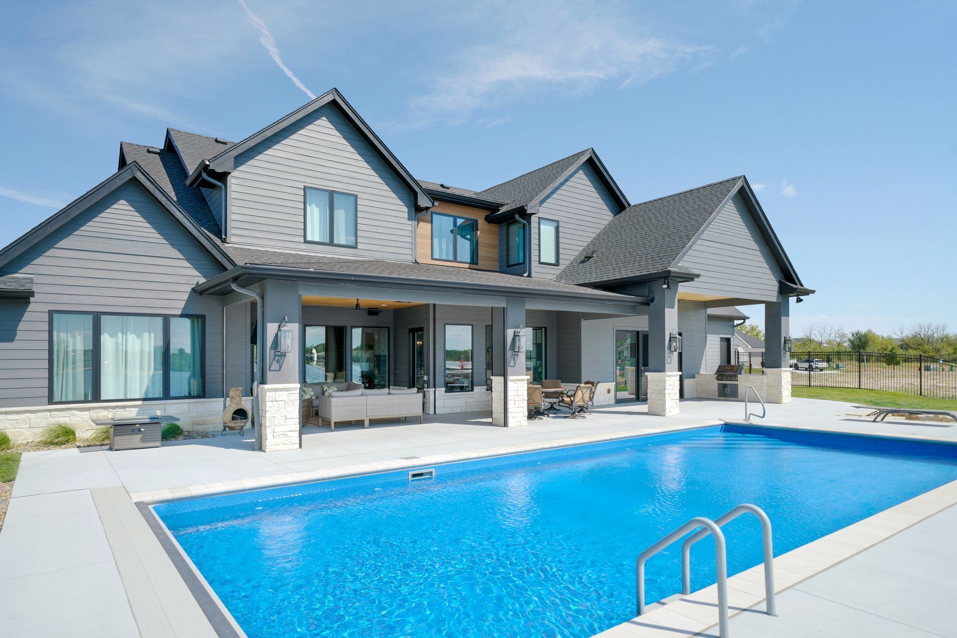 Modern gray house with pool, blue sky. Backyard patio with furniture, clear blue pool.