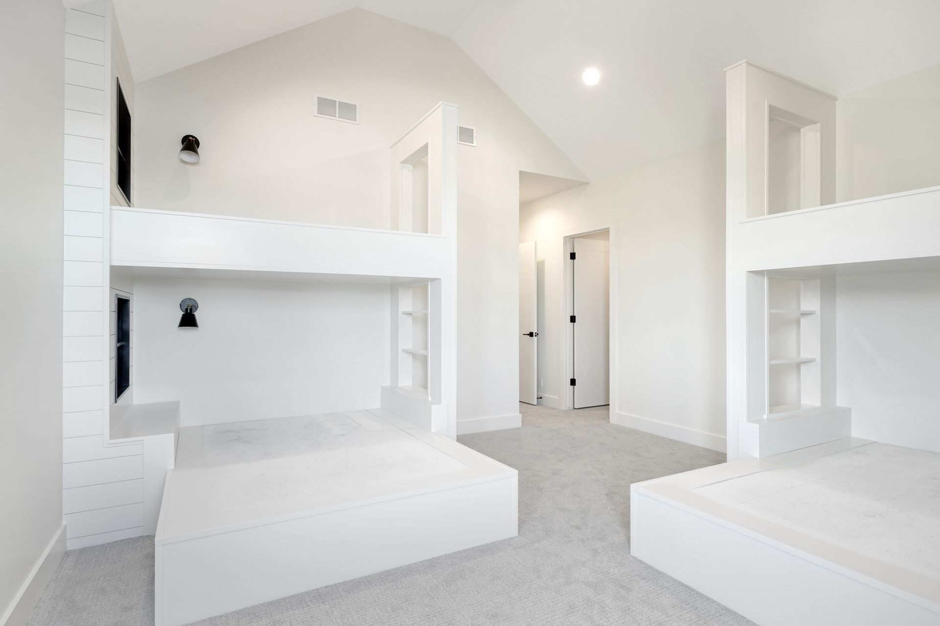 White bunk beds in a bright room with a light gray carpet and a door in the background.
