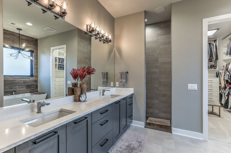 Modern bathroom with dual sinks, gray cabinets, and a walk-in closet.