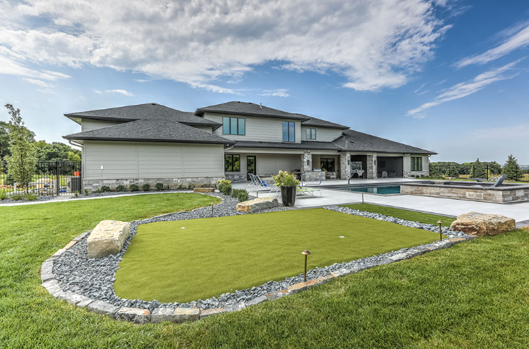 Large modern house with a putting green, pool, and patio on a sunny day.