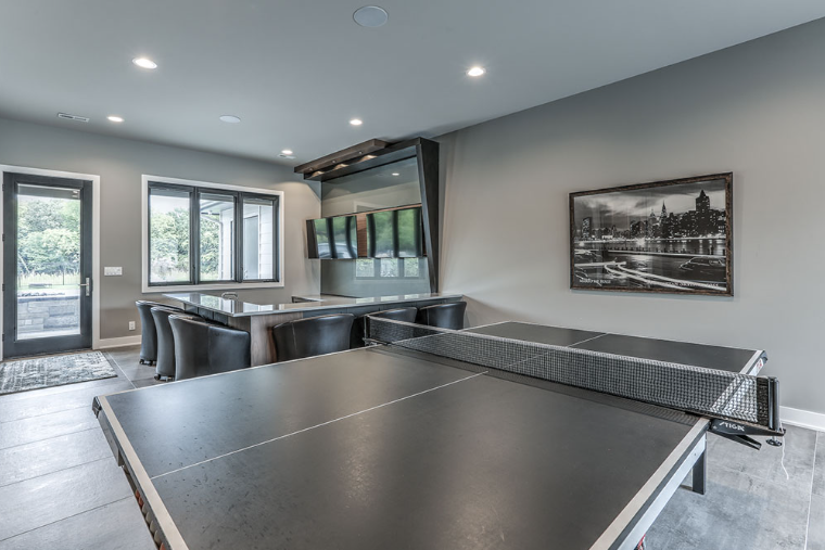 Game room with ping pong table, bar, and multiple TV screens. Gray walls, modern design.