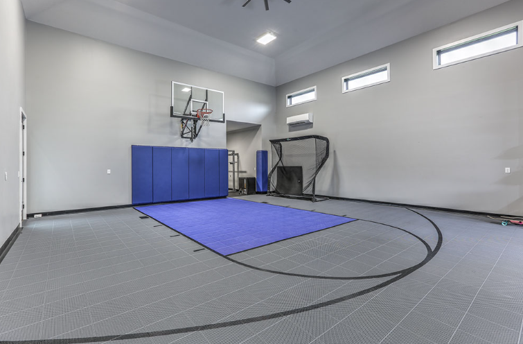 Indoor sports court with basketball hoop, training net, and blue mat on gray floor.
