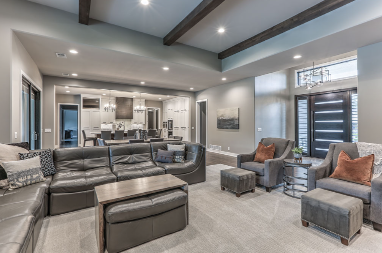 Spacious living room with gray furniture, kitchen in the background, and a modern front door.