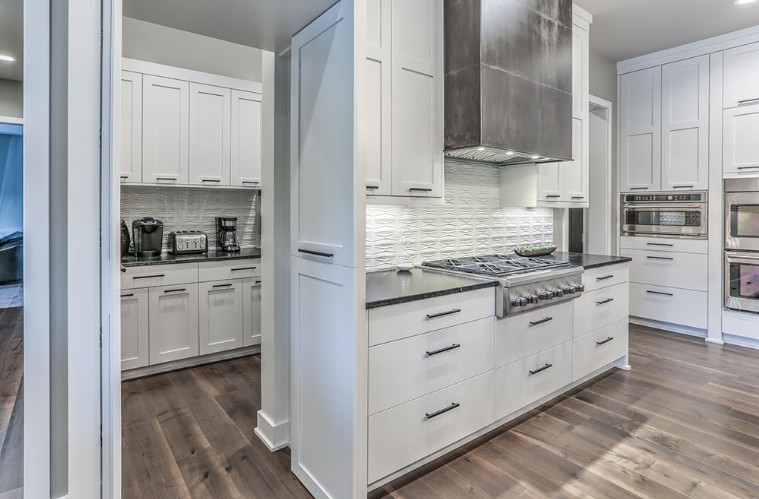 Modern white kitchen with dark countertops, stainless steel appliances, and wood flooring.