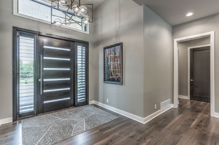 Modern entryway with dark wood door, sidelights, gray walls, artwork, and hardwood flooring.