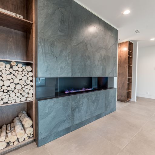 Modern fireplace with gray stone surround, built-in log storage, and wood shelving.