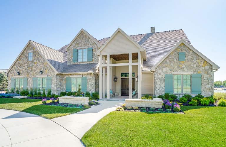 Stone-clad house with pale blue shutters, walkway, and well-maintained lawn under a sunny sky.