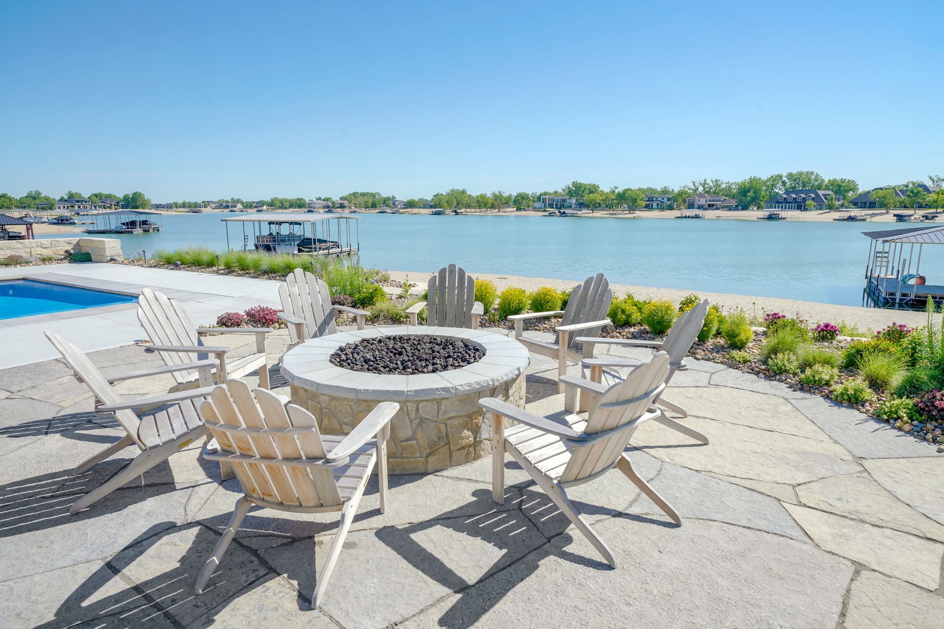 Patio with fire pit and Adirondack chairs overlooking a lake with boats.