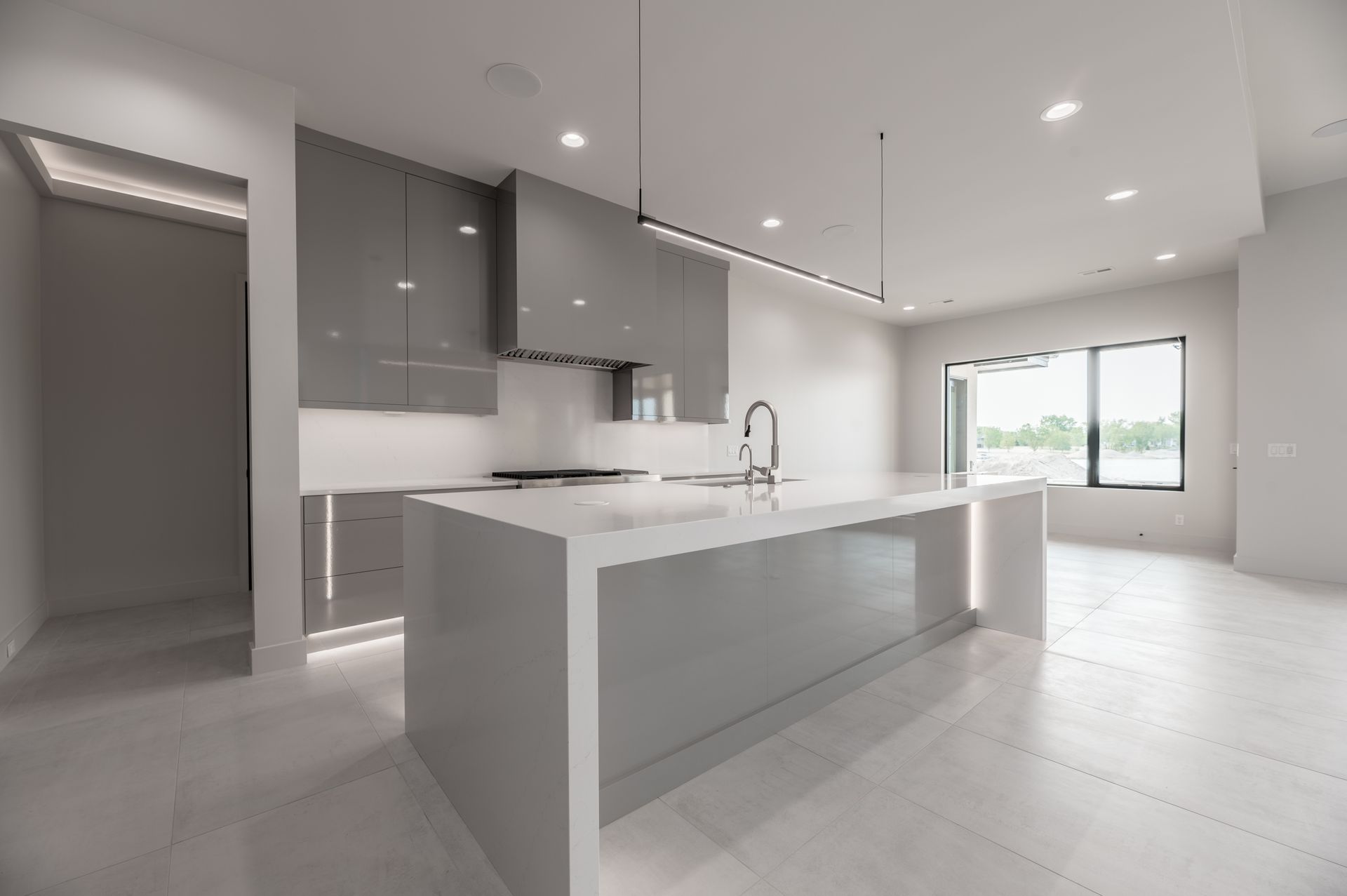 Modern kitchen with gray cabinetry, white island, and large window.