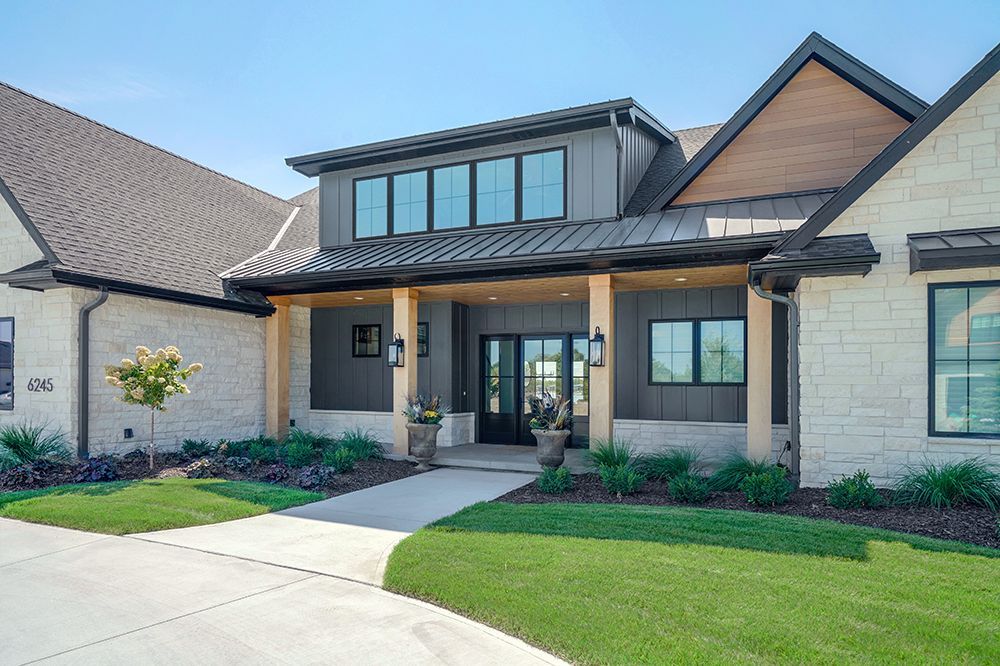 Modern home exterior with gray siding, stone facade, and a walkway leading to the front door.