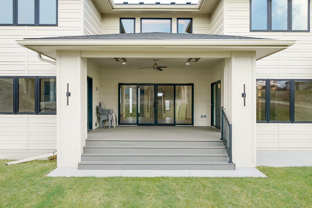Beige house with covered porch, sliding glass doors, steps, and green lawn.