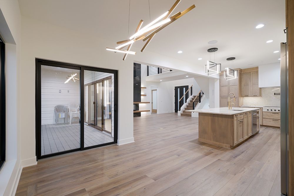 Open-plan modern kitchen and living space, featuring wooden floors, large sliding glass doors, and a staircase.